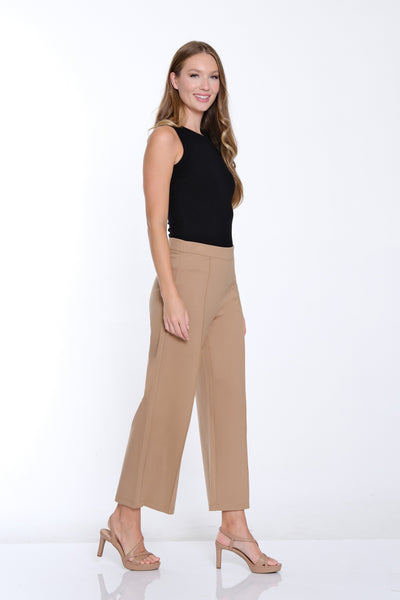 Woman wearing a black sleeveless top and beige high-waisted pants on a white background